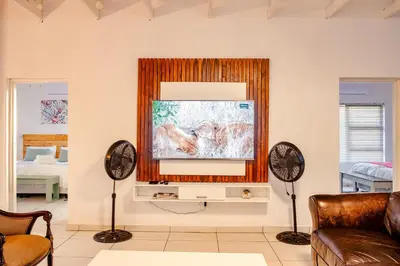 a living room with a flat screen tv and two fans at Gemsbok Place in Marloth Park