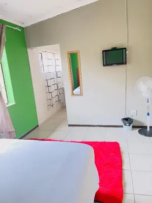 a room with a red rug and a tv on a wall at Galaxy Guest House Pretoria in Pretoria
