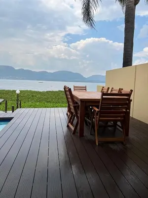 a wooden table and chairs on a deck with the water at Pecanwood Dam View in Hartbeespoort