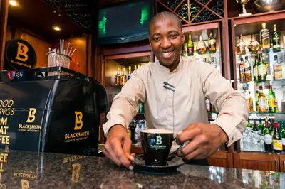 a man standing behind a bar holding a coffee cup at aha Kopanong Hotel & Conference Centre in Bredell