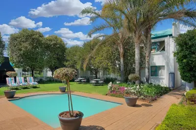 a swimming pool with palm trees and a house at Protea Hotel by Marriott Polokwane Landmark in Polokwane
