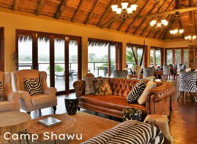 a living room with couches and chairs and windows at Shishangeni Lodge In Kruger National Park in Komatipoort