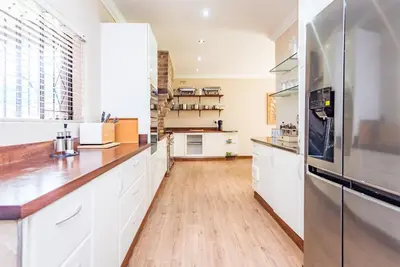 a kitchen with white cabinets and a wooden floor at 150 Jacaranda Guesthouse in Midrand