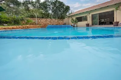 a large swimming pool with blue water in front of a house at Three Oaks and an Aloe Boutique Hotel in Hartbeespoort