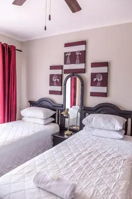 two beds in a bedroom with red curtains at Tzaneen Arborpark Lodge in Tzaneen
