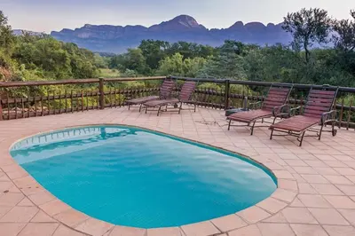 a swimming pool on a patio with chairs and mountains at Amazing mountain views! Solar powered! in Hoedspruit