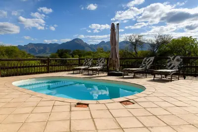 a swimming pool with two chairs and an umbrella at Amazing mountain views! Solar powered! in Hoedspruit