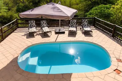 a blue swimming pool with chairs and an umbrella at Amazing mountain views! Solar powered! in Hoedspruit