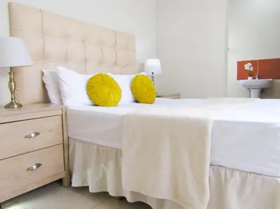 a bedroom with a white bed with yellow pillows at Khaya Guesthouse in Soshanguve