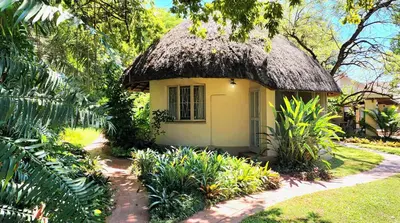 a small yellow house with a thatched roof at Kiaat Bungalows in Hazyview