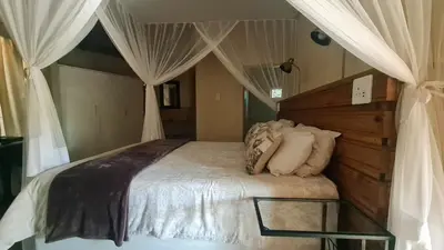 a bedroom with a canopy bed with white curtains at Kiaat Bungalows in Hazyview