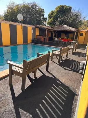 a swimming pool with two benches in front of a building at Platinum Guesthouse Kempton park in Kempton Park