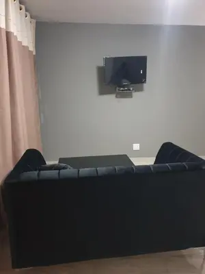 a black couch in a living room with a tv at Platinum Guesthouse Kempton park in Kempton Park
