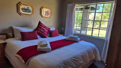 a bed with red and white pillows and a window at Apple Blossom Cottage in Dullstroom