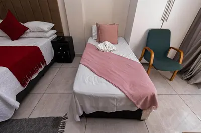 a small bedroom with two beds and a chair at Mandulia Guest House in Nelspruit