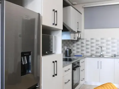 a kitchen with a stainless steel refrigerator and white cabinets at Next To Apartment Hotel in Pretoria