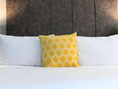 a bed with white pillows and a yellow pillow at Next To Apartment Hotel in Pretoria