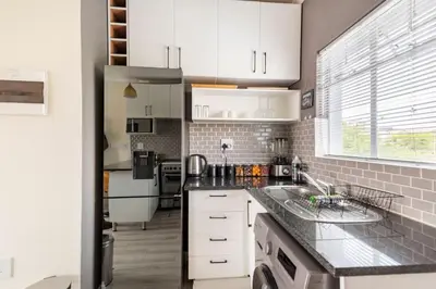 a kitchen with white cabinets and a black counter top at Sunset View Apartment with Free Secure Parking in Central Location in Centurion