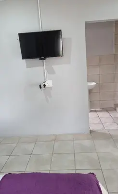a bathroom with a tv on the wall and a purple rug at The Unit Party House in eNyalungu