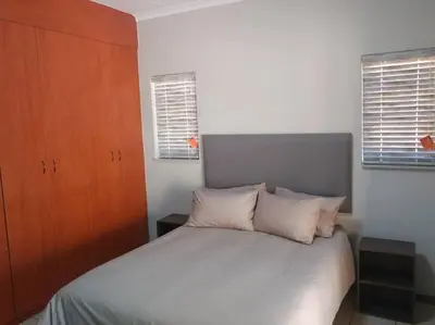 a bedroom with a white bed with a wooden cabinet at Ebeneezer Self-Catering Guesthouse in the Lowveld in Sabie
