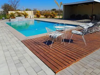 a group of chairs sitting on a wooden deck next to a swimming pool at Mogale Royal Gardens in Polokwane