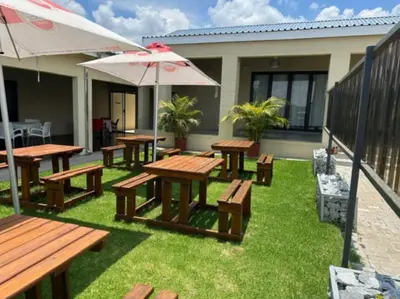 a group of picnic tables with an umbrella and grass at Mogale Royal Gardens in Polokwane