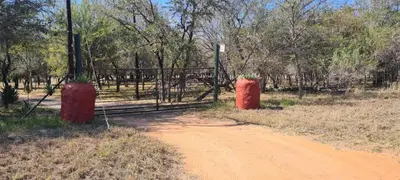 a dirt road with two red cylinders next to a gate at Vanross Self Catering Accommodation in Thabazimbi