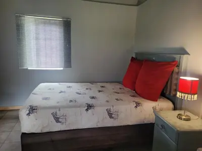 a bedroom with a bed with red pillows and a window at Vanross Self Catering Accommodation in Thabazimbi
