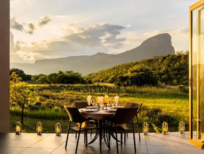a dining table with a view of a field and mountains at Sofala Lodge in Mokopane