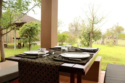 a table with plates and dishes on it with a window at iMbamuweti Cottage in Grietjie Nature Reserve