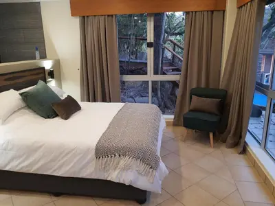 a bedroom with a bed and a chair and a window at Bikkurim Inn in Nelspruit