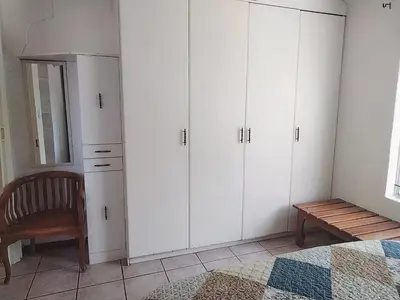 a bedroom with white cabinets and a chair and a table at HomeSweetHome City Apartment in Nelspruit