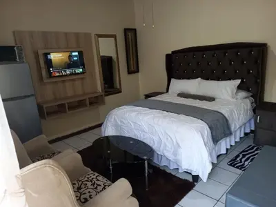 a bedroom with a bed and a tv and two chairs at Mighty7 Bed and Breakfast Guesthouse in Pretoria