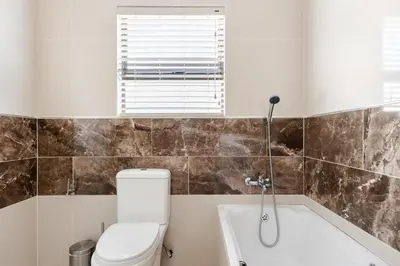 a bathroom with a toilet and a window and a tub at Gosheni Villas in White River