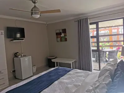 a bedroom with a bed and a tv and a balcony at 19th on Bloekom Guesthouse in Secunda