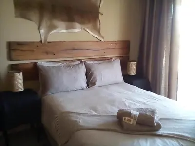 a bedroom with a white bed with a wooden headboard at Nyani Lodge Dinokeng in Pretoria
