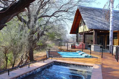 a house with a swimming pool next to a wooden deck at Fish Eagle Villa in Hoedspruit