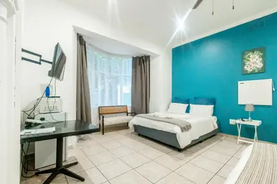 a bedroom with a blue wall with a bed and a desk at 54 Brecher in Pretoria