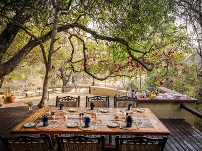 a wooden table with food on a wooden deck with trees at Shimungwe Lodge, Thornybush Game Reserve in Hoedspruit