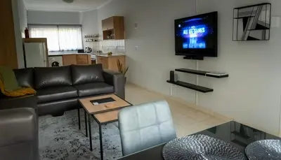 a living room with a couch and a tv on the wall at VillaZek a modern 2 bedroom open- plan apartment with parking in Pretoria