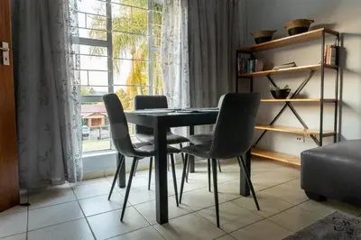 a dining room table with chairs and a window at VillaZek a modern 2 bedroom open- plan apartment with parking in Pretoria
