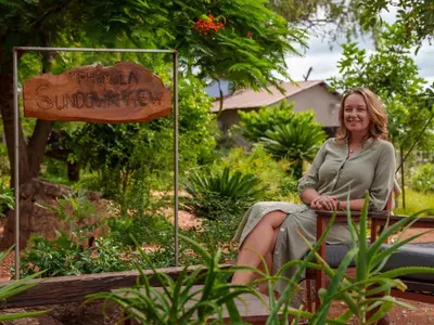 a woman sitting on a bench next to a sign at Phomola Manor Holiday Home in Phalaborwa