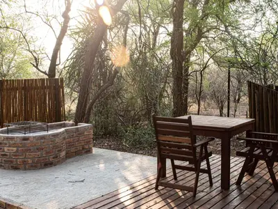 a wooden table and chairs on a deck with a fire pit at Cottage@Injabulo in Marloth Park
