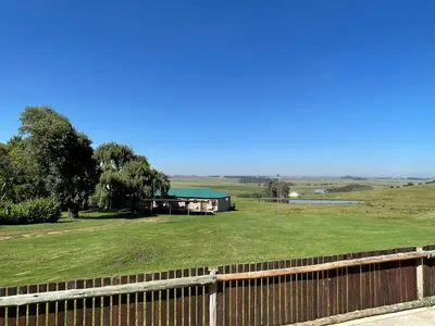 a house in a field with a fence at Holbank River Lodge in Ermelo