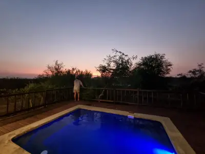 a man standing on a deck next to a blue pool at Stoep At Kruger in Komatipoort