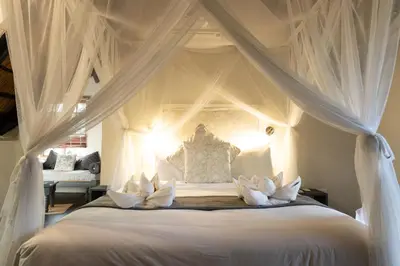 a bedroom with a white canopy bed with white pillows at Braai Safaris Lodge in Hoedspruit