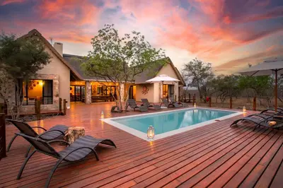 a pool on a wooden deck with chairs and a house at Vuyani Marula Lodge in Hoedspruit