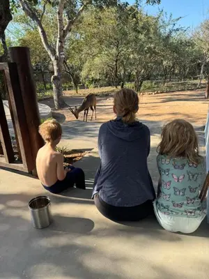 three people sitting on the ground looking at a deer at Greater Kruger View - Luxury Bush Villa in Marloth Park
