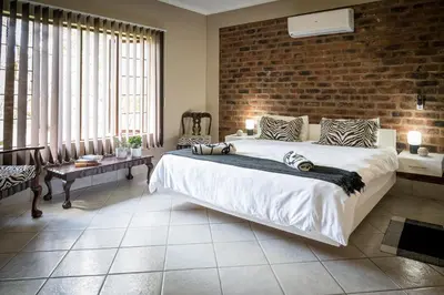a bedroom with a large bed and a brick wall at Bosveld Villa in Marloth Park