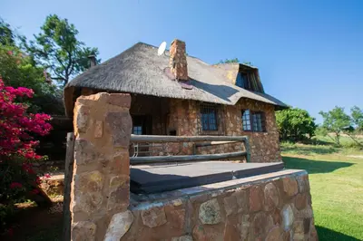 a small stone house with a thatched roof at Koraalboom at Benlize in Hartbeespoort